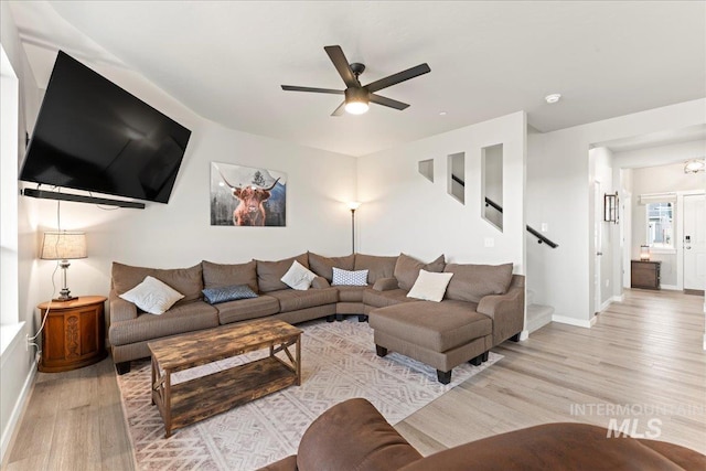 living area featuring light wood finished floors, ceiling fan, stairs, and baseboards