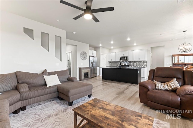 living room featuring a glass covered fireplace, light wood-style flooring, recessed lighting, and ceiling fan with notable chandelier