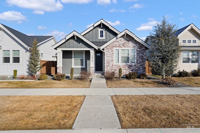 view of front of home featuring brick siding, board and batten siding, a front lawn, and fence