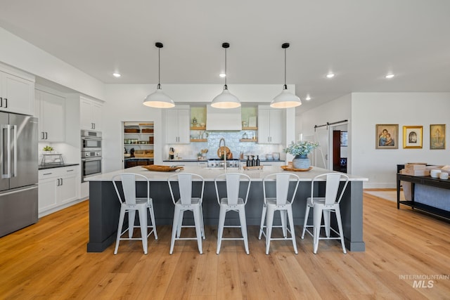 1305 N Big Star Pl, Eagle, ID 83616 - kitchen featuring appliances with stainless steel finishes, a barn door, decorative backsplash, white cabinets, and light wood-style floors