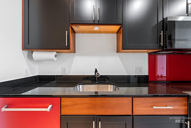 kitchen with stainless steel microwave, a sink, and dark stone countertops