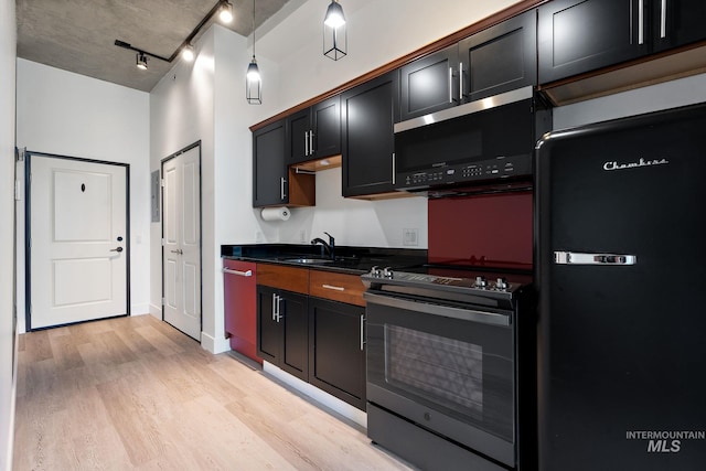 kitchen with a sink, light wood-style floors, black appliances, dark countertops, and track lighting