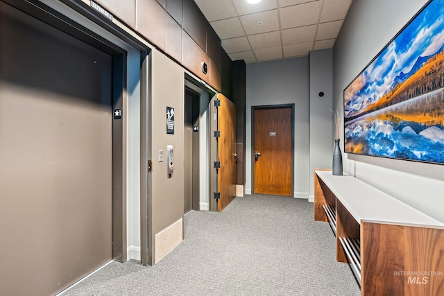 hall featuring elevator, carpet, baseboards, and a drop ceiling