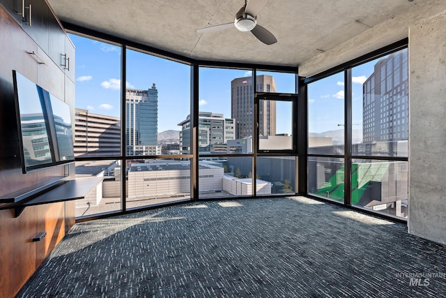 unfurnished sunroom with a healthy amount of sunlight, a city view, and ceiling fan