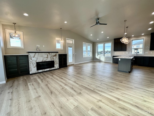 unfurnished living room featuring ceiling fan, a fireplace, vaulted ceiling, and light hardwood / wood-style flooring