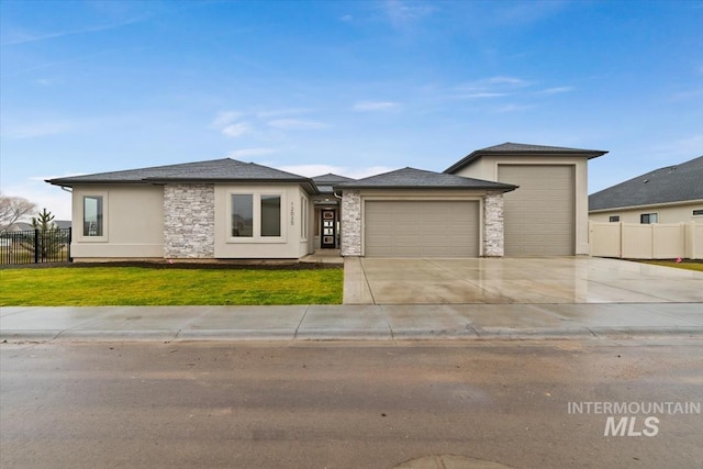 prairie-style house with concrete driveway, fence, a garage, stone siding, and a front lawn