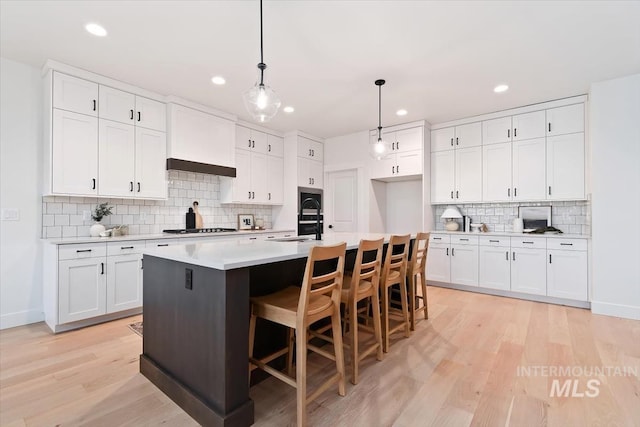 kitchen with pendant lighting, white cabinets, stainless steel gas cooktop, and light wood-style flooring