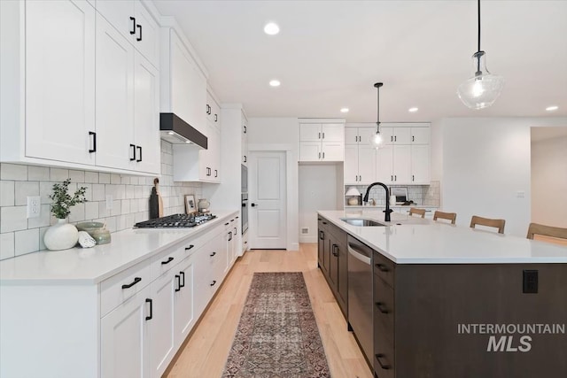 kitchen featuring stainless steel appliances, white cabinetry, a sink, and wall chimney range hood