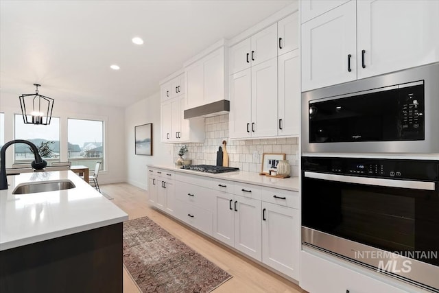 kitchen with stainless steel gas cooktop, light wood finished floors, tasteful backsplash, a sink, and built in microwave