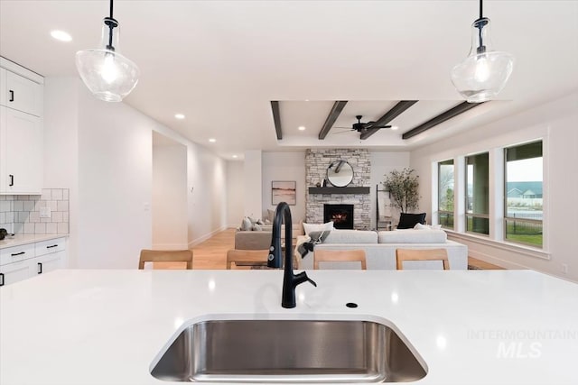 kitchen featuring tasteful backsplash, white cabinets, light countertops, a stone fireplace, and a sink