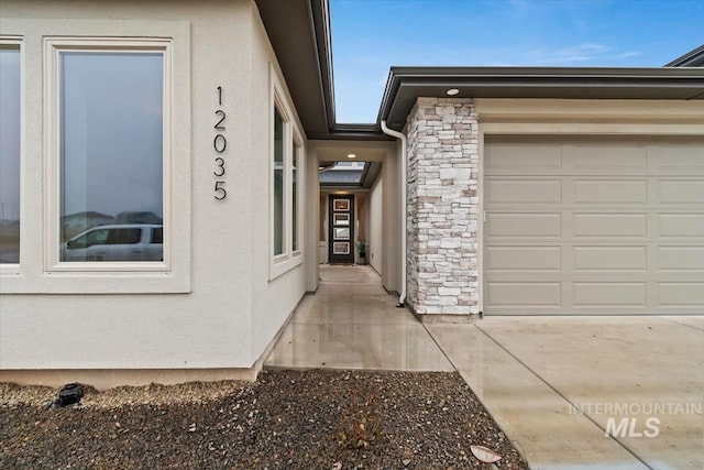 doorway to property featuring an attached garage, stone siding, and stucco siding