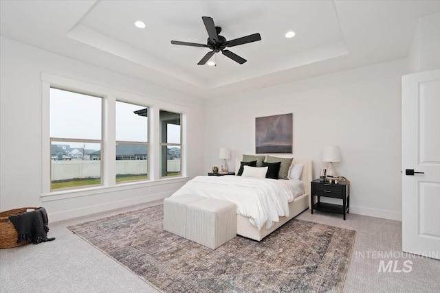 bedroom with a tray ceiling, recessed lighting, light colored carpet, and baseboards