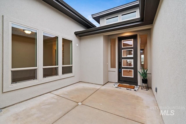 view of exterior entry with a patio and stucco siding