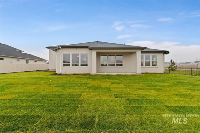 back of house featuring a yard, fence, and stucco siding