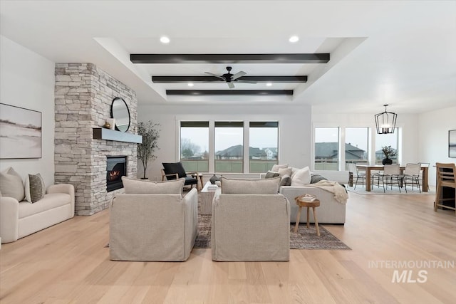 living area with ceiling fan with notable chandelier, a fireplace, wood finished floors, and beam ceiling