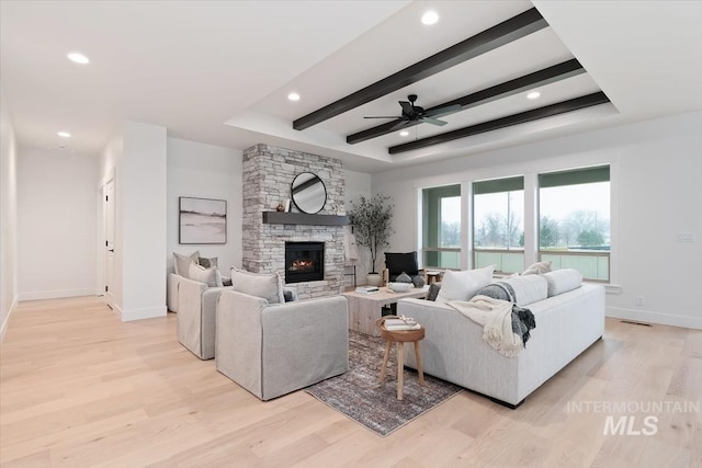 living room featuring a stone fireplace, light wood-style flooring, recessed lighting, baseboards, and beam ceiling