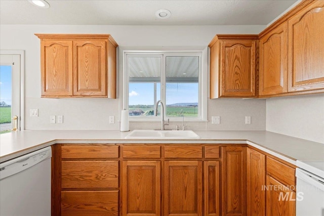 kitchen with light countertops, dishwasher, brown cabinets, and a sink