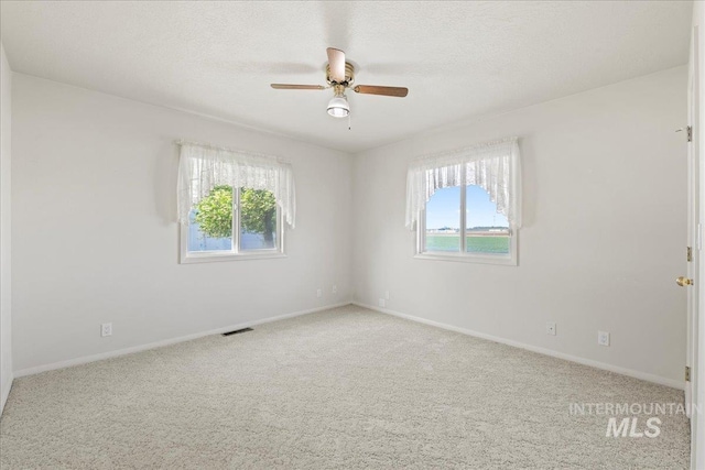 carpeted spare room with baseboards, visible vents, ceiling fan, and a healthy amount of sunlight