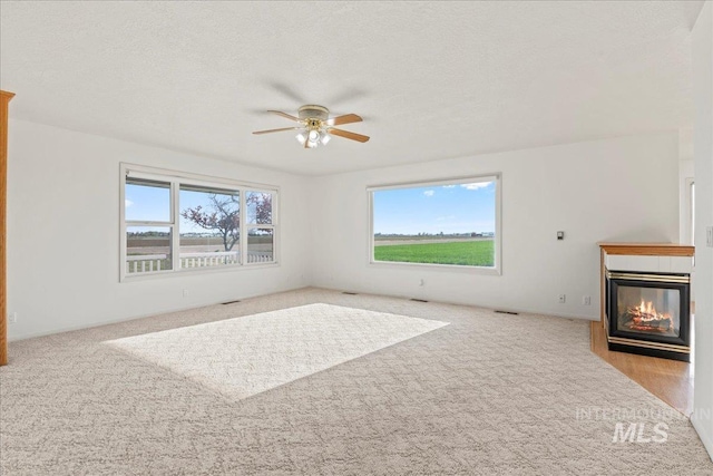 unfurnished living room featuring ceiling fan, carpet flooring, a multi sided fireplace, and a textured ceiling
