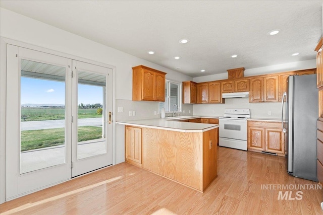 kitchen with a peninsula, freestanding refrigerator, light wood-style floors, under cabinet range hood, and electric stove