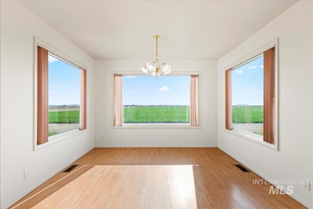 empty room featuring wood finished floors, visible vents, baseboards, and an inviting chandelier