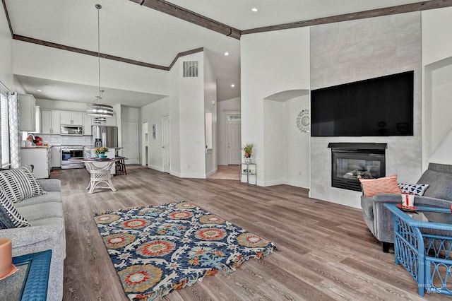 living area featuring a tiled fireplace, high vaulted ceiling, light wood finished floors, and baseboards
