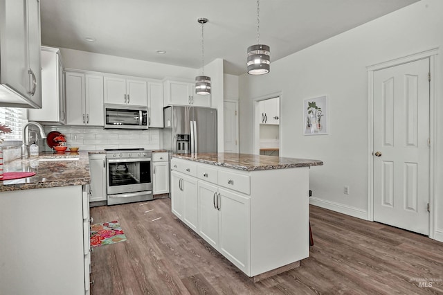 kitchen with appliances with stainless steel finishes, dark stone counters, wood finished floors, and tasteful backsplash