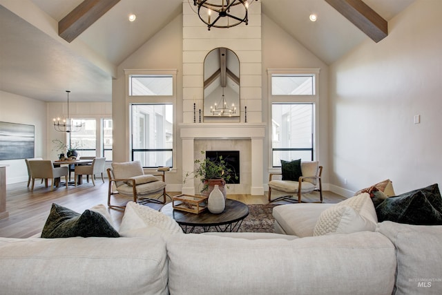 living area with a chandelier, high vaulted ceiling, beamed ceiling, light wood-style floors, and a tile fireplace