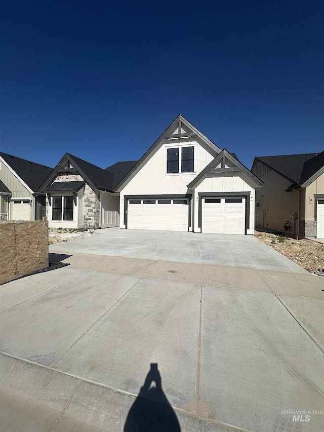 modern farmhouse featuring board and batten siding, concrete driveway, a garage, and stone siding