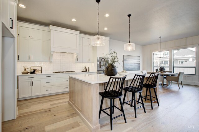 kitchen featuring gas cooktop, light countertops, backsplash, light wood finished floors, and premium range hood
