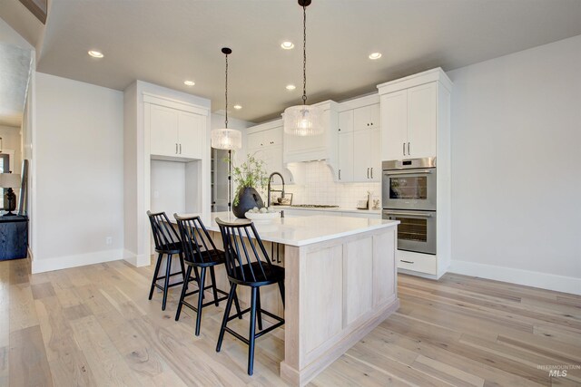 kitchen featuring stainless steel double oven, decorative backsplash, light wood-style floors, light countertops, and recessed lighting