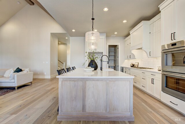 kitchen featuring stainless steel appliances, a sink, decorative backsplash, light wood-style floors, and baseboards