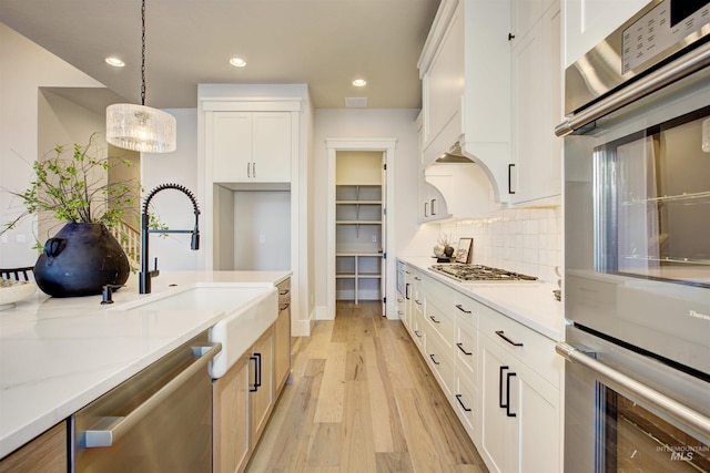 kitchen with stainless steel appliances, light wood-style floors, hanging light fixtures, tasteful backsplash, and white cabinetry