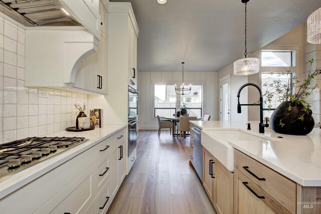 kitchen featuring a sink, stainless steel appliances, light wood-style floors, decorative backsplash, and pendant lighting
