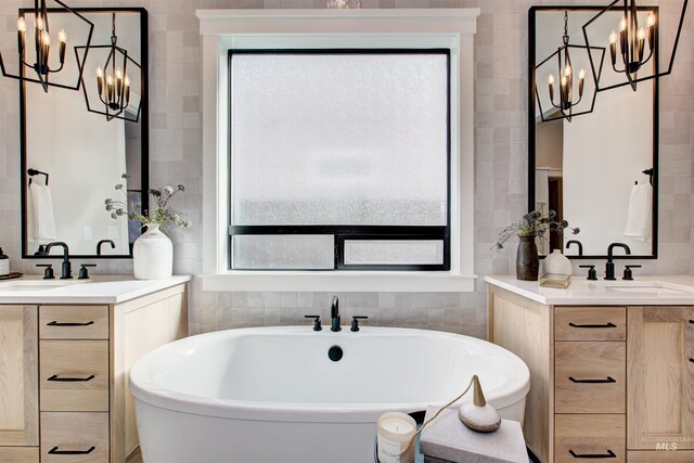 bathroom with a chandelier, two vanities, tile walls, and a soaking tub