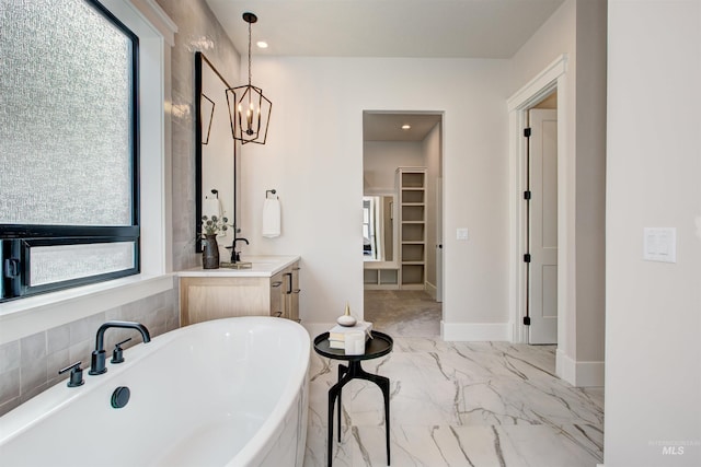 full bath with marble look tiles, healthy amount of natural light, a freestanding tub, a spacious closet, and recessed lighting