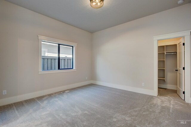 unfurnished bedroom featuring carpet flooring, a walk in closet, baseboards, and a closet