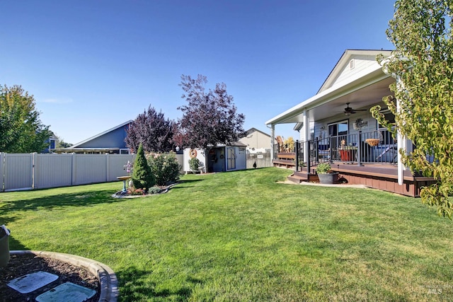 view of yard featuring a storage shed, ceiling fan, a fenced backyard, an outdoor structure, and a wooden deck