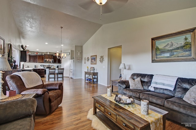 living area featuring ceiling fan with notable chandelier, high vaulted ceiling, dark wood-style flooring, and baseboards