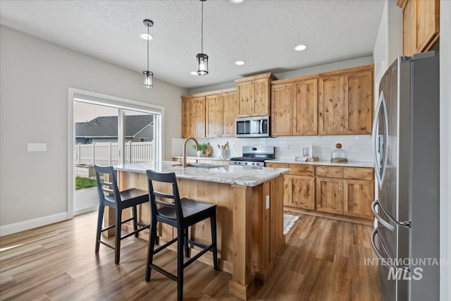 2065 Sombrero Ave, Middleton, ID 83644 - kitchen featuring appliances with stainless steel finishes, backsplash, wood finished floors, a kitchen island with sink, and pendant lighting