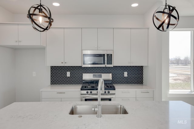 kitchen with tasteful backsplash, light stone countertops, appliances with stainless steel finishes, white cabinetry, and pendant lighting