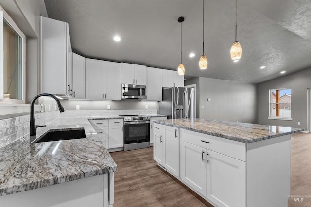 kitchen with sink, hanging light fixtures, a kitchen island, white cabinets, and appliances with stainless steel finishes