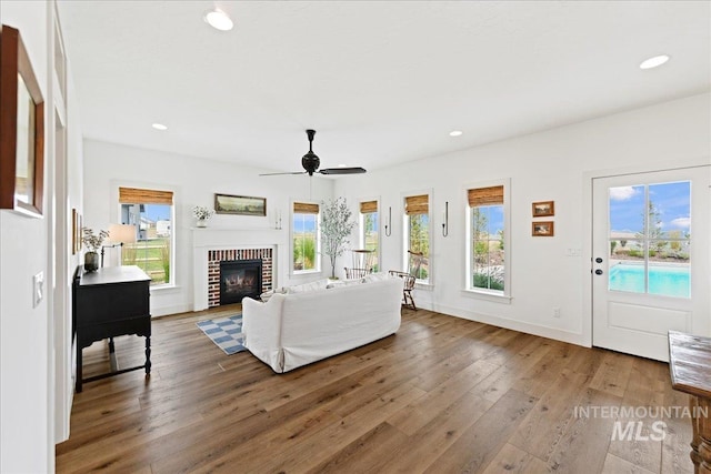 living room with recessed lighting, baseboards, wood-type flooring, and a brick fireplace