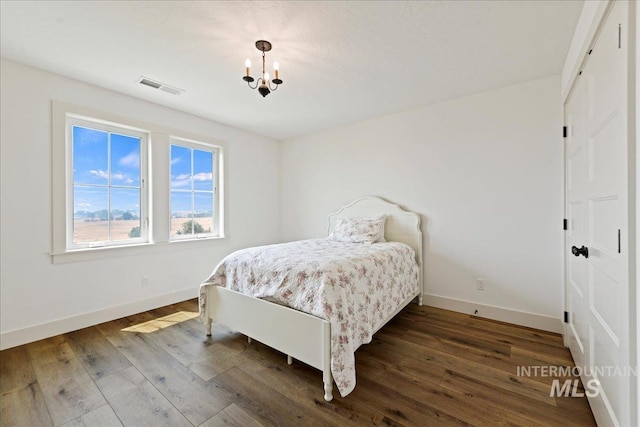 bedroom featuring visible vents, baseboards, an inviting chandelier, and wood finished floors