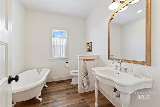 bathroom with visible vents, toilet, wood finished floors, baseboards, and a soaking tub