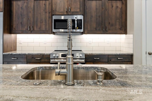 kitchen featuring light stone counters, stainless steel appliances, dark brown cabinets, and backsplash