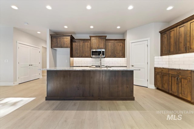 kitchen featuring an island with sink, light stone counters, and light hardwood / wood-style floors