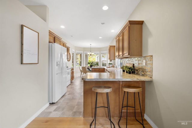 380 S Golden Eagle Ln, Eagle, ID 83616 - kitchen featuring white refrigerator with ice dispenser, a peninsula, brown cabinets, light countertops, and a chandelier