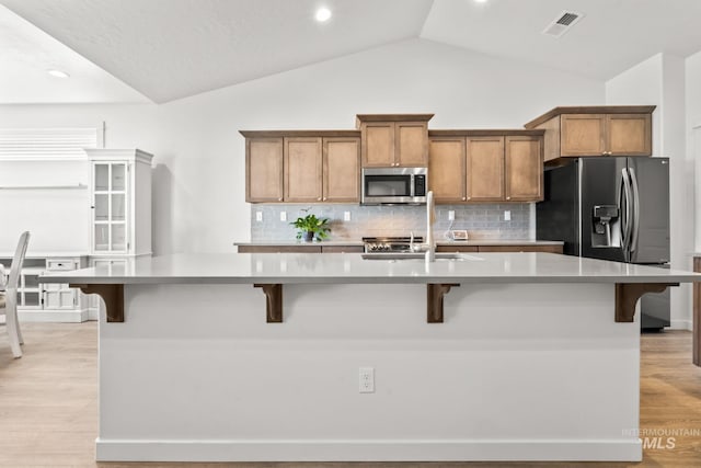 kitchen with stainless steel appliances, brown cabinets, tasteful backsplash, lofted ceiling, and a sink