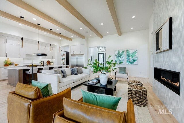 living room featuring beamed ceiling, light wood-type flooring, a large fireplace, and sink